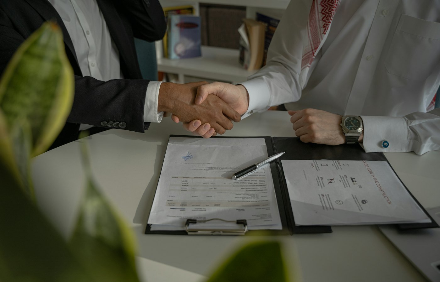 Duas pessoas apertando as mãos sobre documentos durante a formalização de um contrato